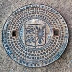 manhole cover, sieldeckel, coat of arms of schleswig-holstein, metal, split, on the left, two lions, right holstein nettle leaf, cover, sewage system, wastewater, gullideckel, plate, custom-made